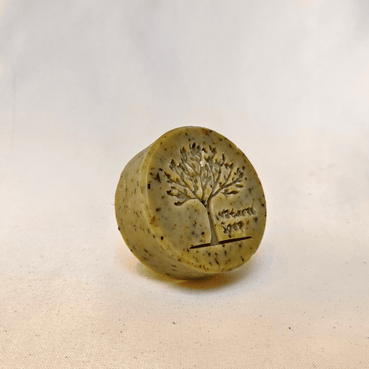 Rund, mat grøn sæbe med et aftryk af et træ. 